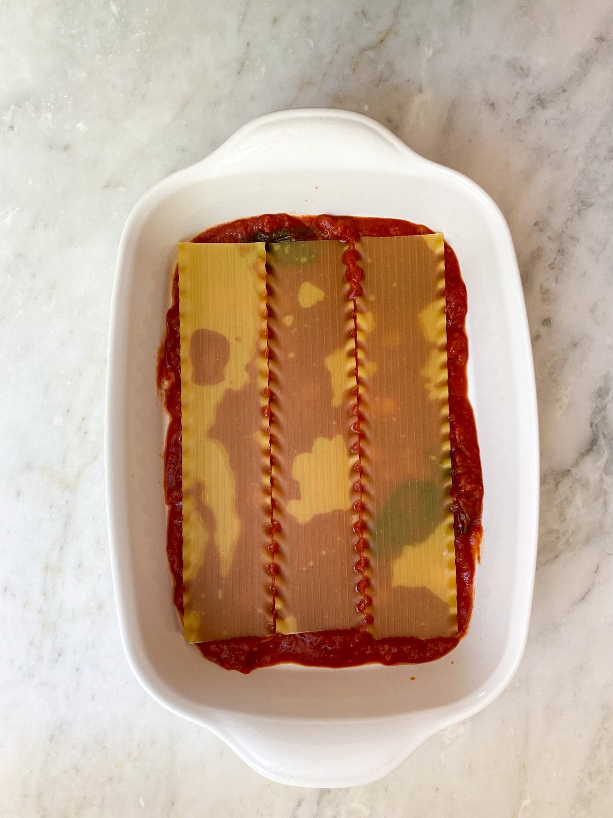 layering the lasagna noodles on top of sauce.