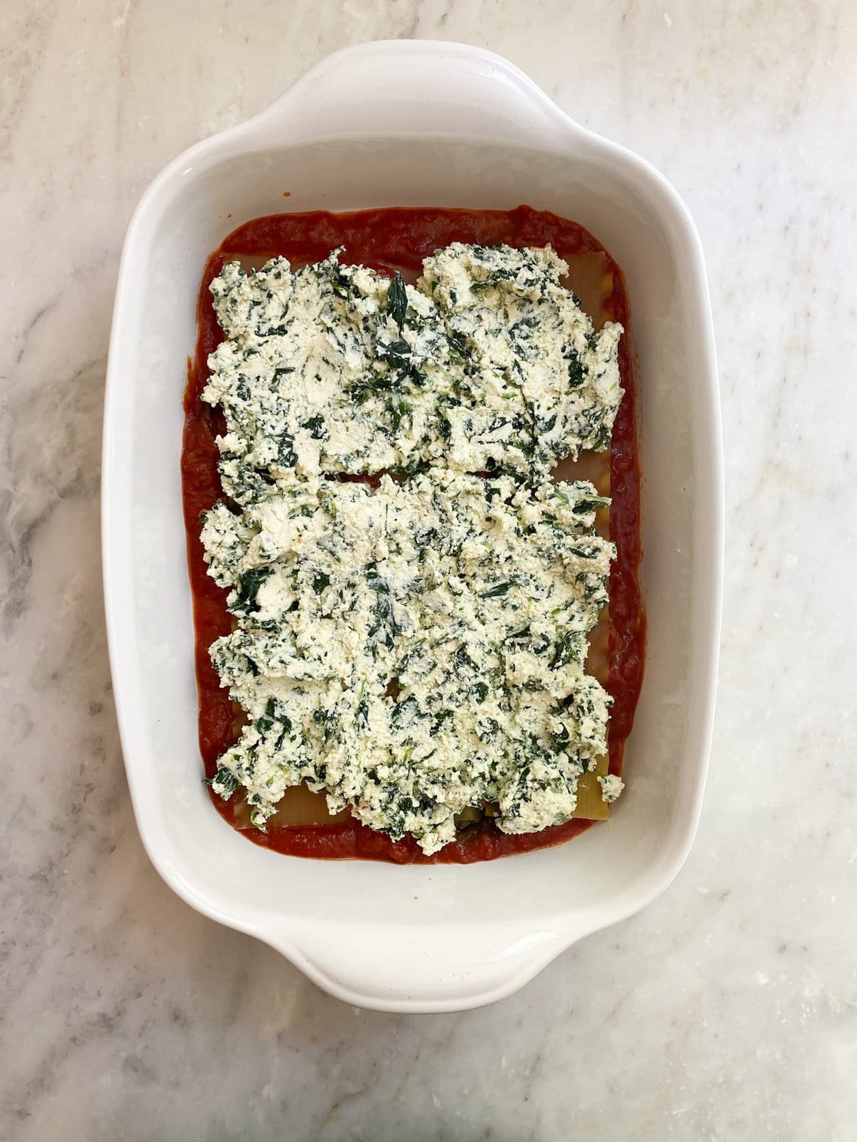 layering the spinach and  ricotta filling on top of noodles and sauce. 