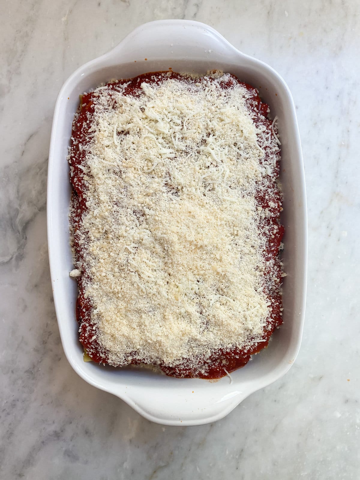 Layered noodles and sauce topped with cheese in a baking dish.
