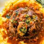 osso buco on a white plate that served on top of polenta, with sauce, and gremolata.