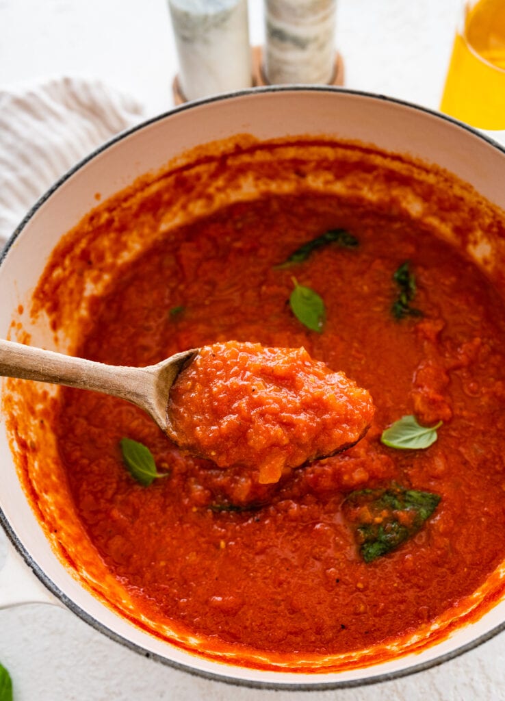wooden spoon inside the pot of Italian tomato sauce and stirring.