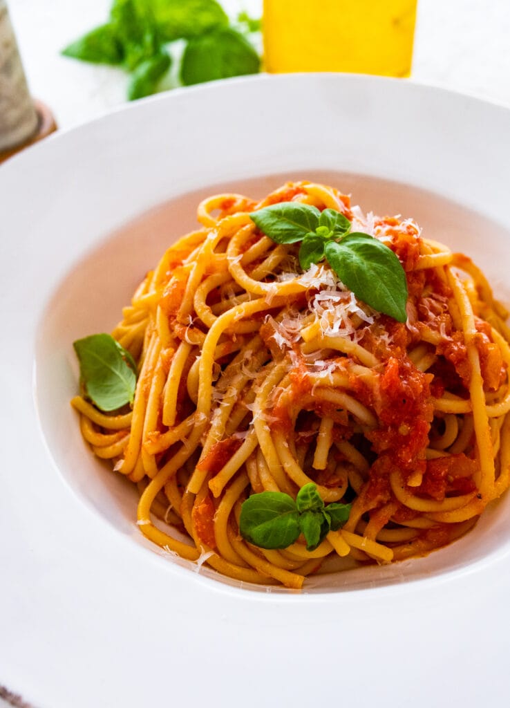 pasta al sugo using this Italian tomato sauce recipe. Pasta plated in a white bowl with basil leaves on top.