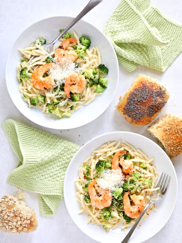 Two plates of shrimp and broccoli pasta in cream sauce.