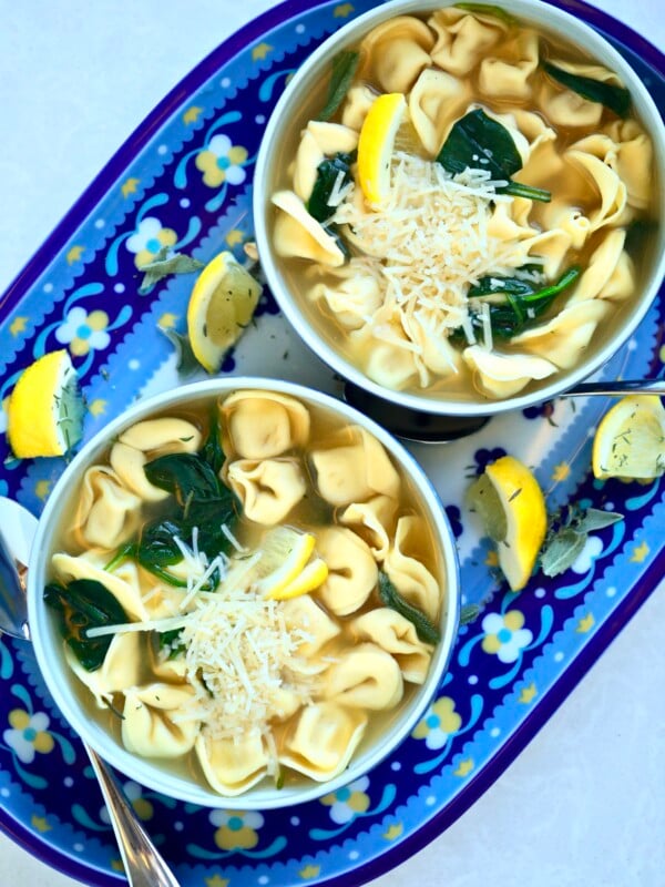 Two bowls of cheese tortellini in broth with spinach on a tray.