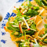 Lemon arugula salad in parmesan cups on a blue and white platter.