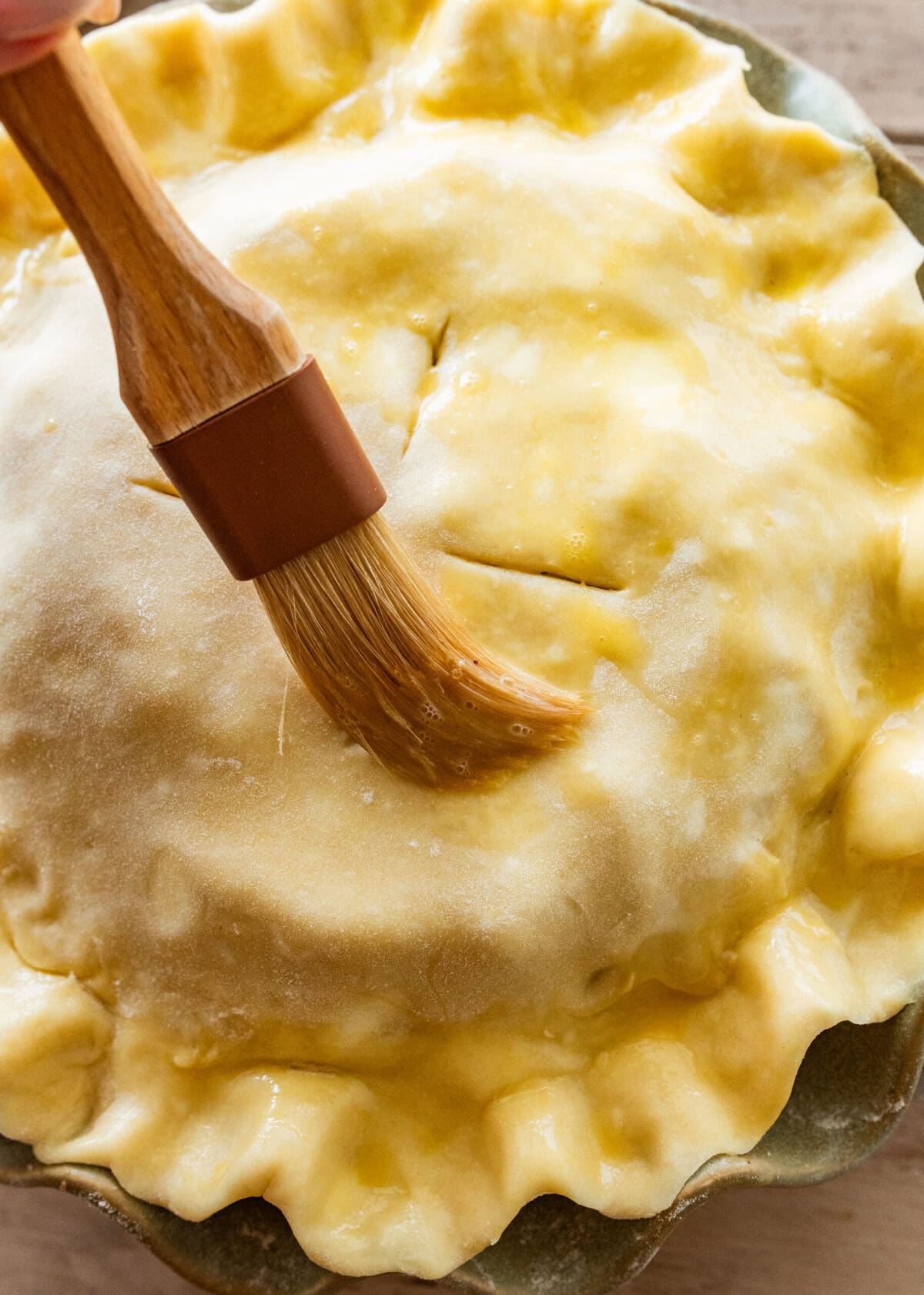 Brushing egg on the top of the pie crust.