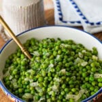 a large serving bowl of frozen peas with a spoon resting inside.
