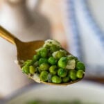 a scoop of peas being held up above the skillet.