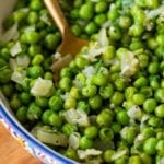 a large serving bowl of frozen peas with a spoon resting inside.