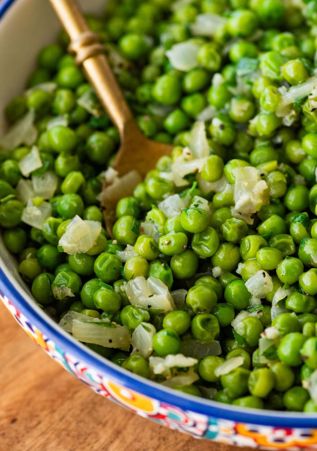 a large serving bowl of frozen peas with a spoon resting inside.