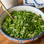 a large serving bowl of frozen peas with a spoon resting inside.