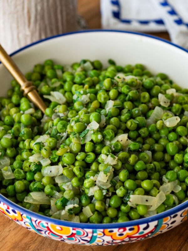 a large serving bowl of frozen peas with a spoon resting inside.