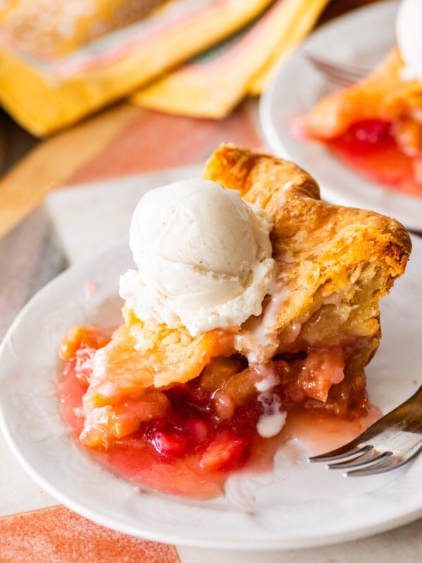 a slice of rhubarb pie on a plate, topped with ice cream with a fork and more pie nearby.