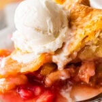 a slice of rhubarb pie on a plate, topped with ice cream with a fork nearby.