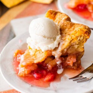 a slice of rhubarb pie on a plate, topped with ice cream with a fork nearby.