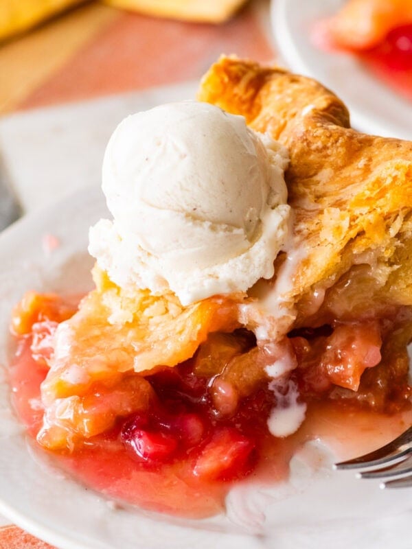 a slice of rhubarb pie on a plate, topped with ice cream with a fork nearby.
