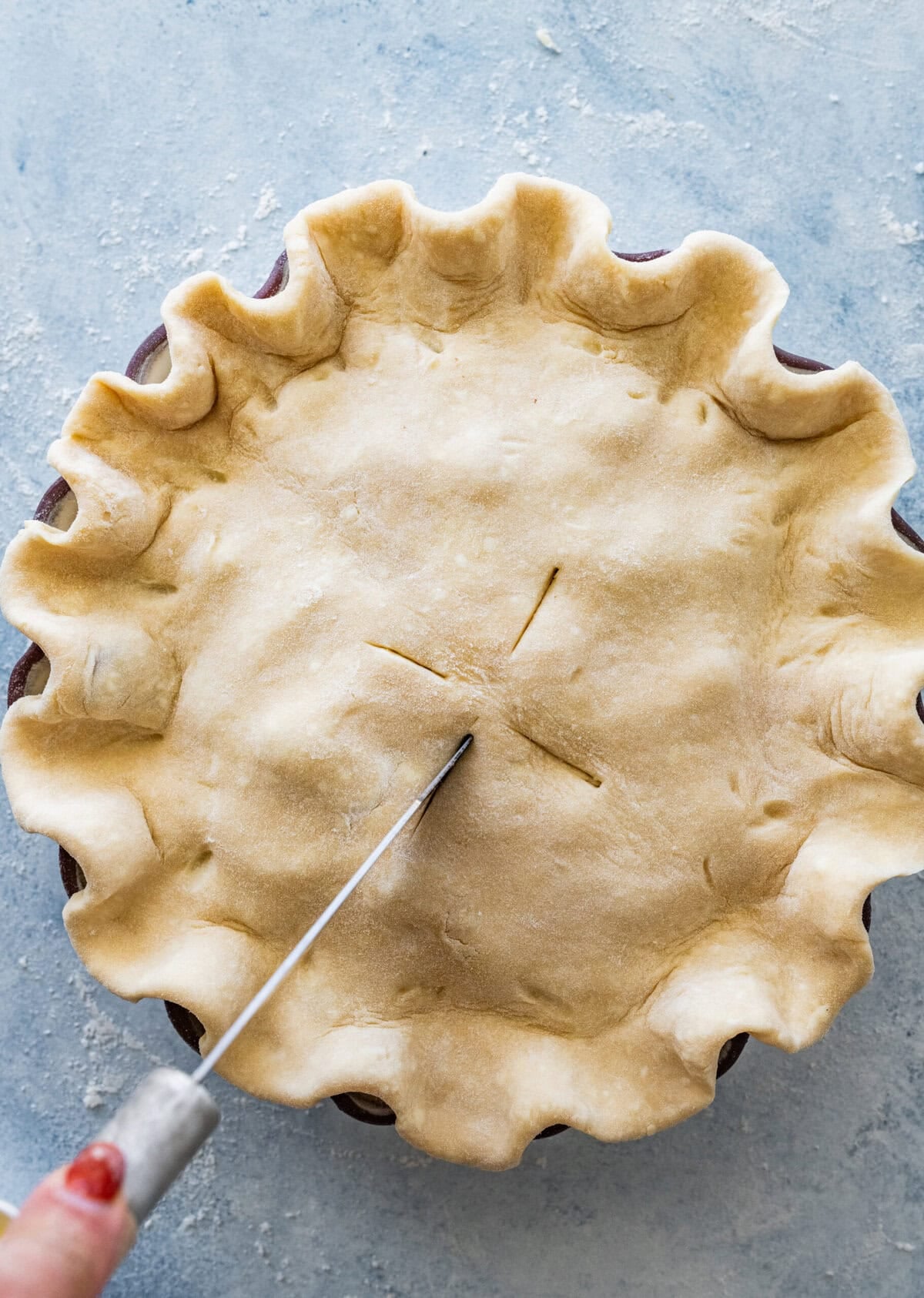 a knife scoring the top of the pie crust.
