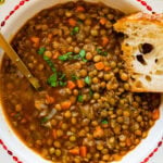a beautiful antique looking bowl full of the classic italian lentils. A golden spoon on the side. A spoon full of the soup ready to eat. A piece of bread dunked in the soup.