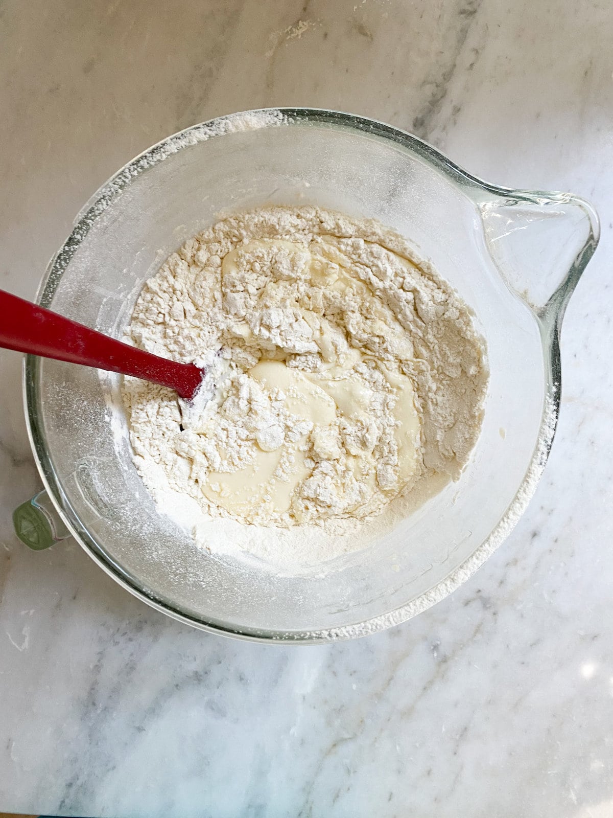 Spoon mixing wet and dry ingredients in a glass bowl.