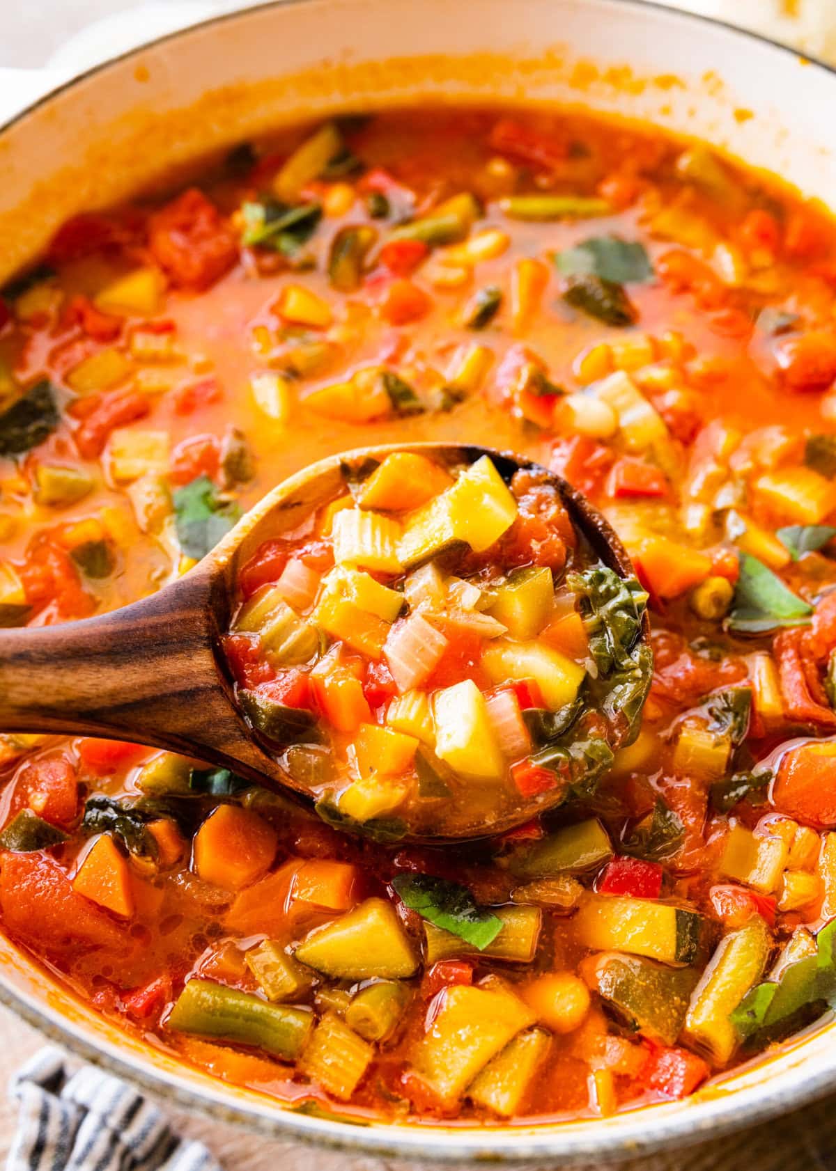 cooked minestrone soup stir with a wooden spoon. Wooden spoon holding some of the minestrone soup.