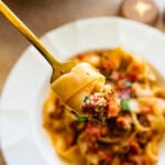 Ragu sauce with pasta in a white serving bowl with a fork on the side.