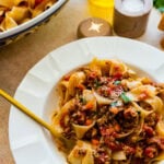 Ragu sauce with pasta in a white serving bowl with a fork in the bowl twirling the pasta.