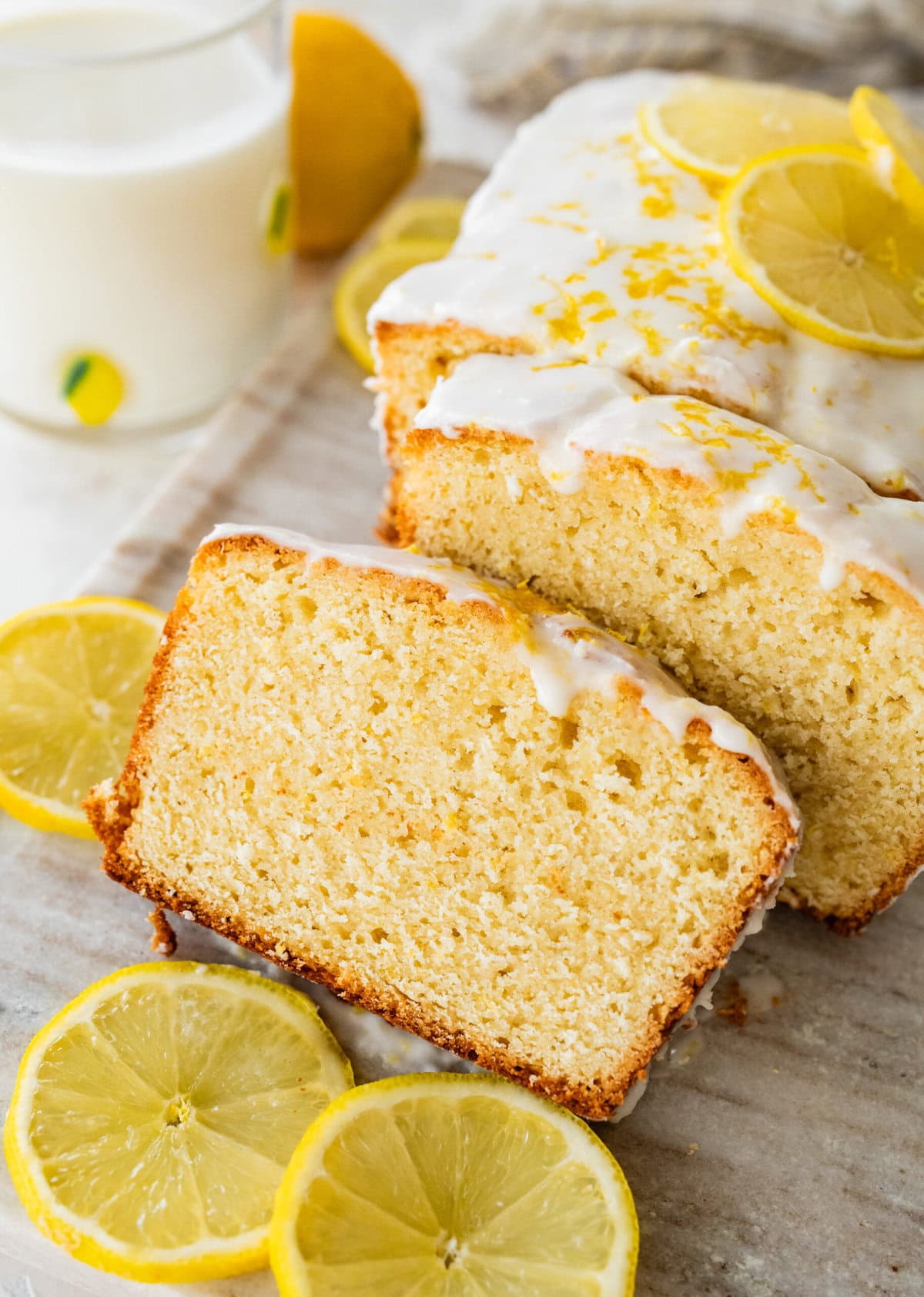A lemon loaf on a wire rack with slices cut and leaning over. 