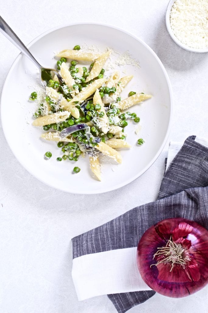 Simple pasta and peas with mascarpone cheese on a white plate with a fork.