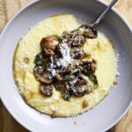 Spoon on a plate with polenta and mushrooms with sage butter sauce.