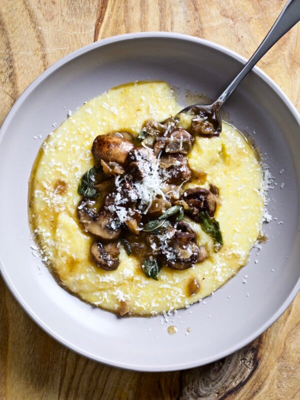 Spoon on a plate with polenta and mushrooms with sage butter sauce.