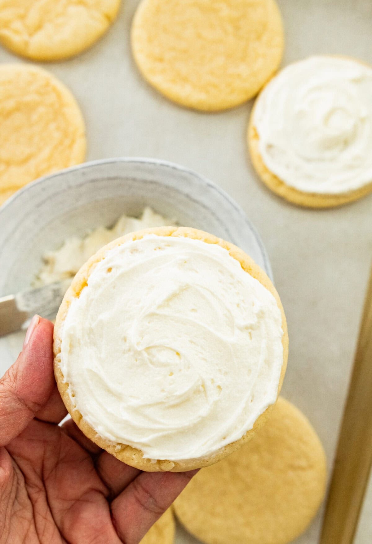 Adding frosting to top of a soft sugar cookie.