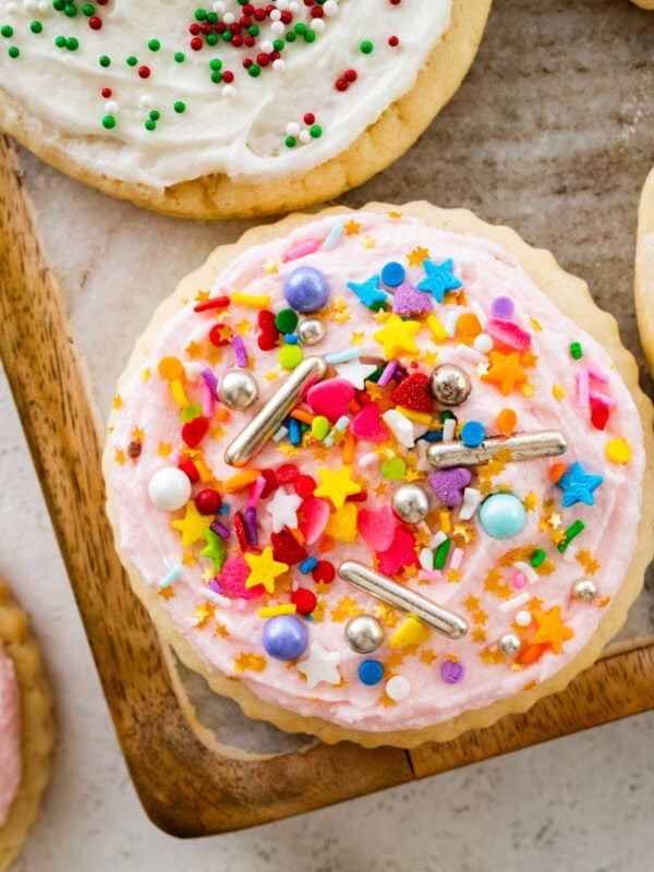 Soft sugar cookies with frosting on a plate topped with colored sprinkles.
