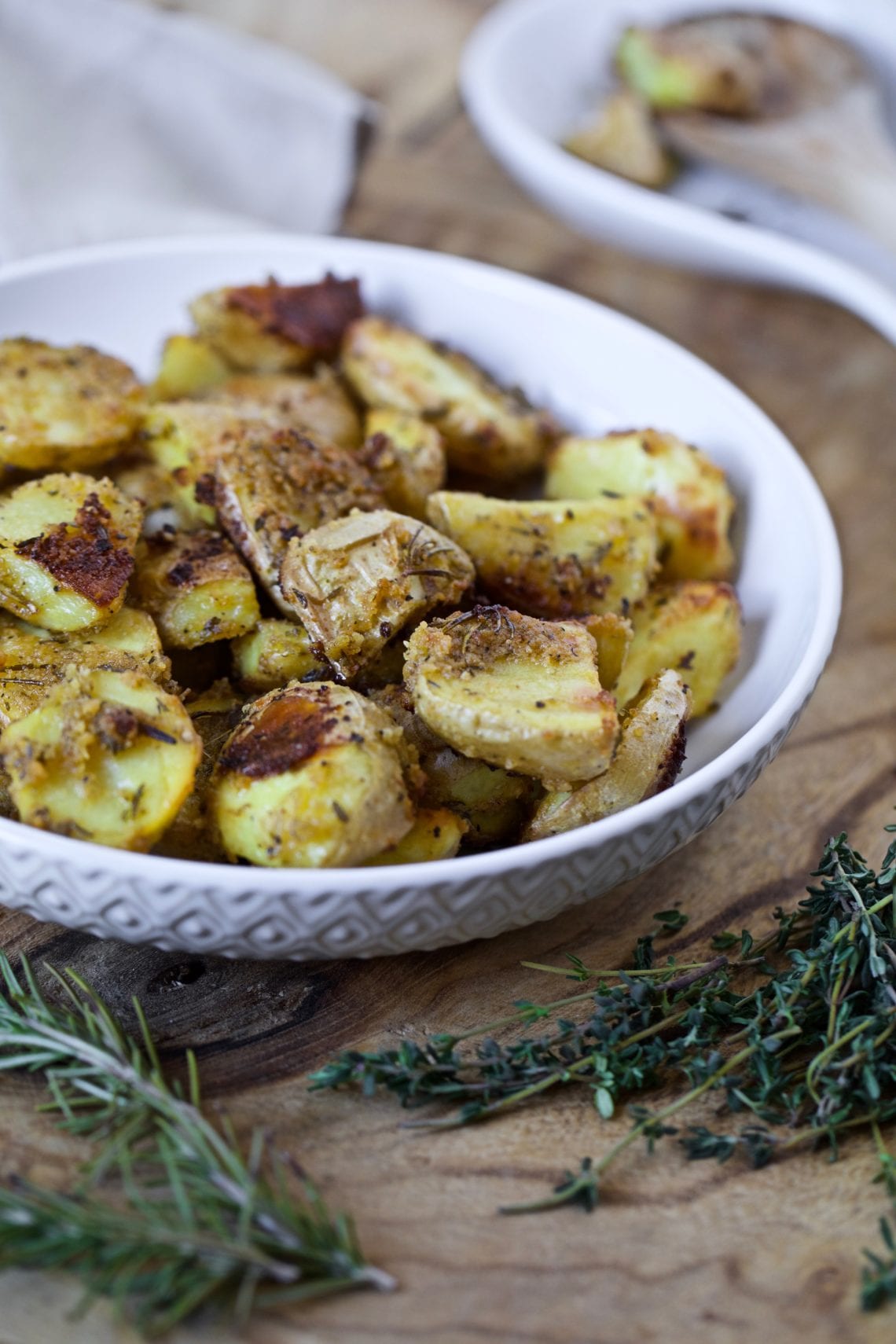 oven roasted potatoes with a crispy exterior and herbs placed in a white bowl on a wooden board
