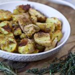 oven roasted potatoes with a crispy exterior and herbs placed in a white bowl on a wooden board