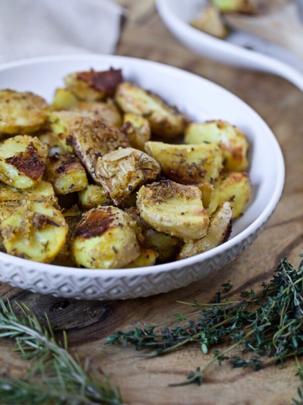 oven roasted potatoes with a crispy exterior and herbs placed in a white bowl on a wooden board