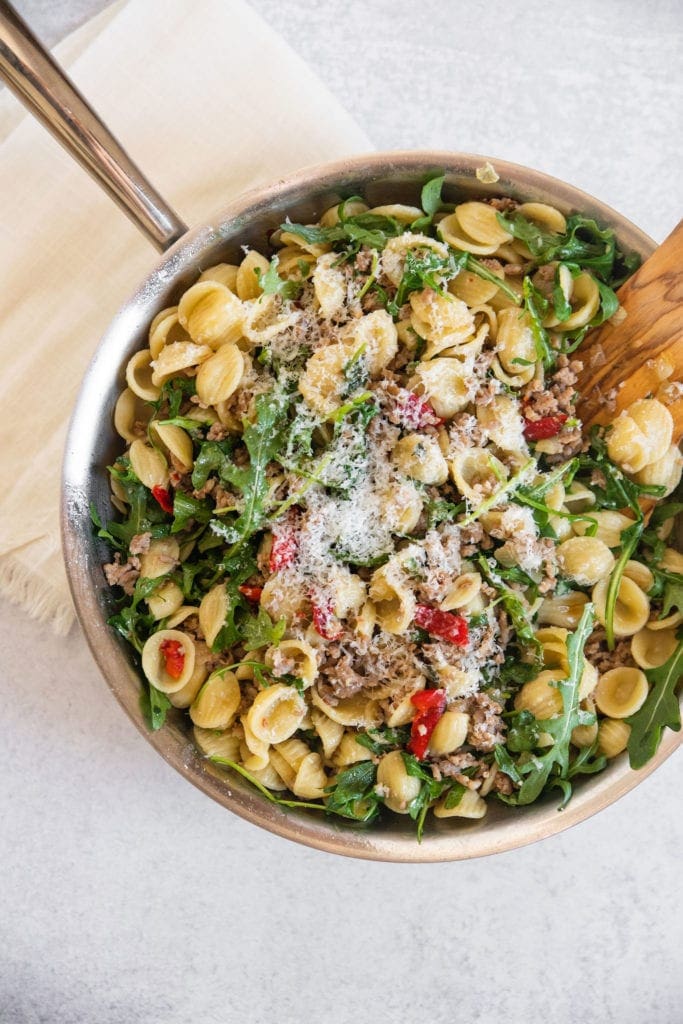 platted final dish of pasta and sausage with arugula and red peppers in a pan with wooden spoon