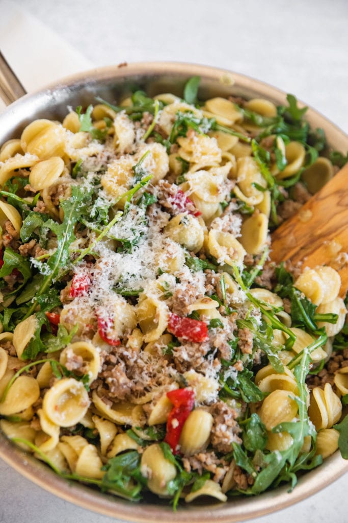 platted final dish of pasta and sausage with arugula and red peppers in a pan with wooden spoon