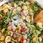 platted final dish of pasta and sausage with arugula and red peppers in a pan with wooden spoon