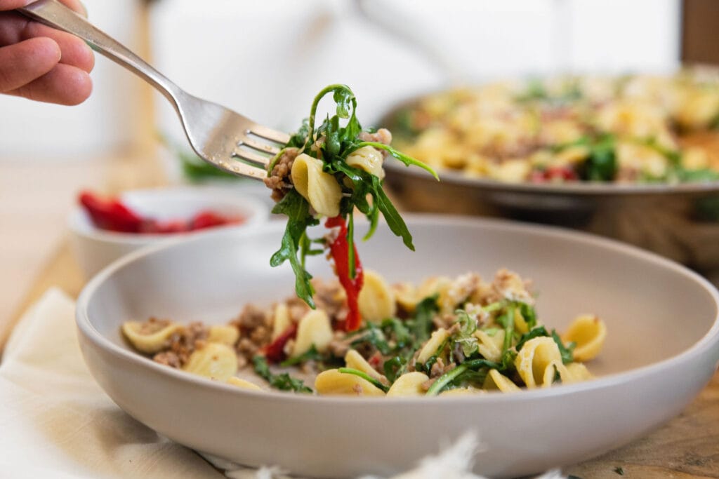 a fork taking a bite of the final plate with pasta and red pepper arugula in the bite