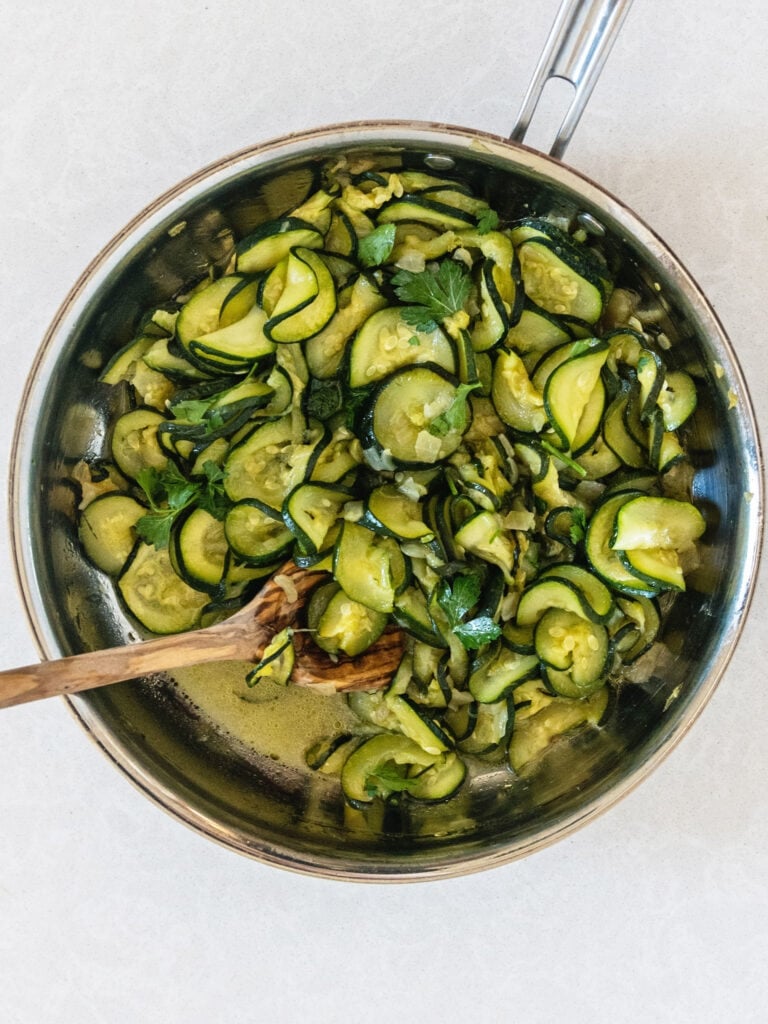 zucchini and onion in a pan with a wooden spoon