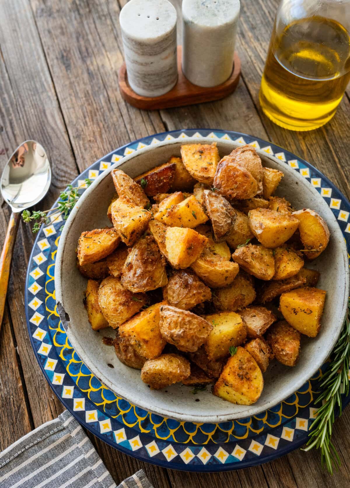 A bowl of Italian roasted potatoes with more recipe ingredients nearby.