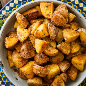 A bowl of Italian roasted potatoes with more recipe ingredients nearby.