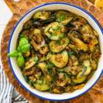 A skillet of sauteed zucchini with onions garnished with basil and parsley.