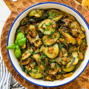 A skillet of sauteed zucchini with onions garnished with basil and parsley.