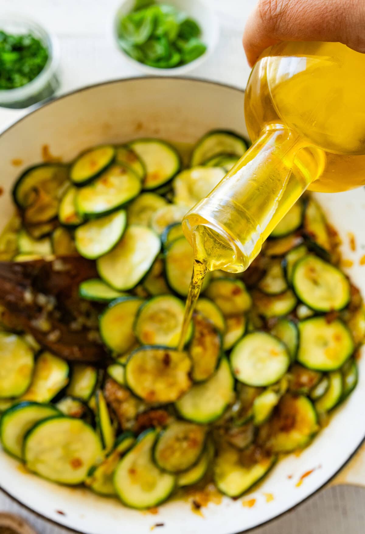Pouring olive oil into the skillet with the zucchini.