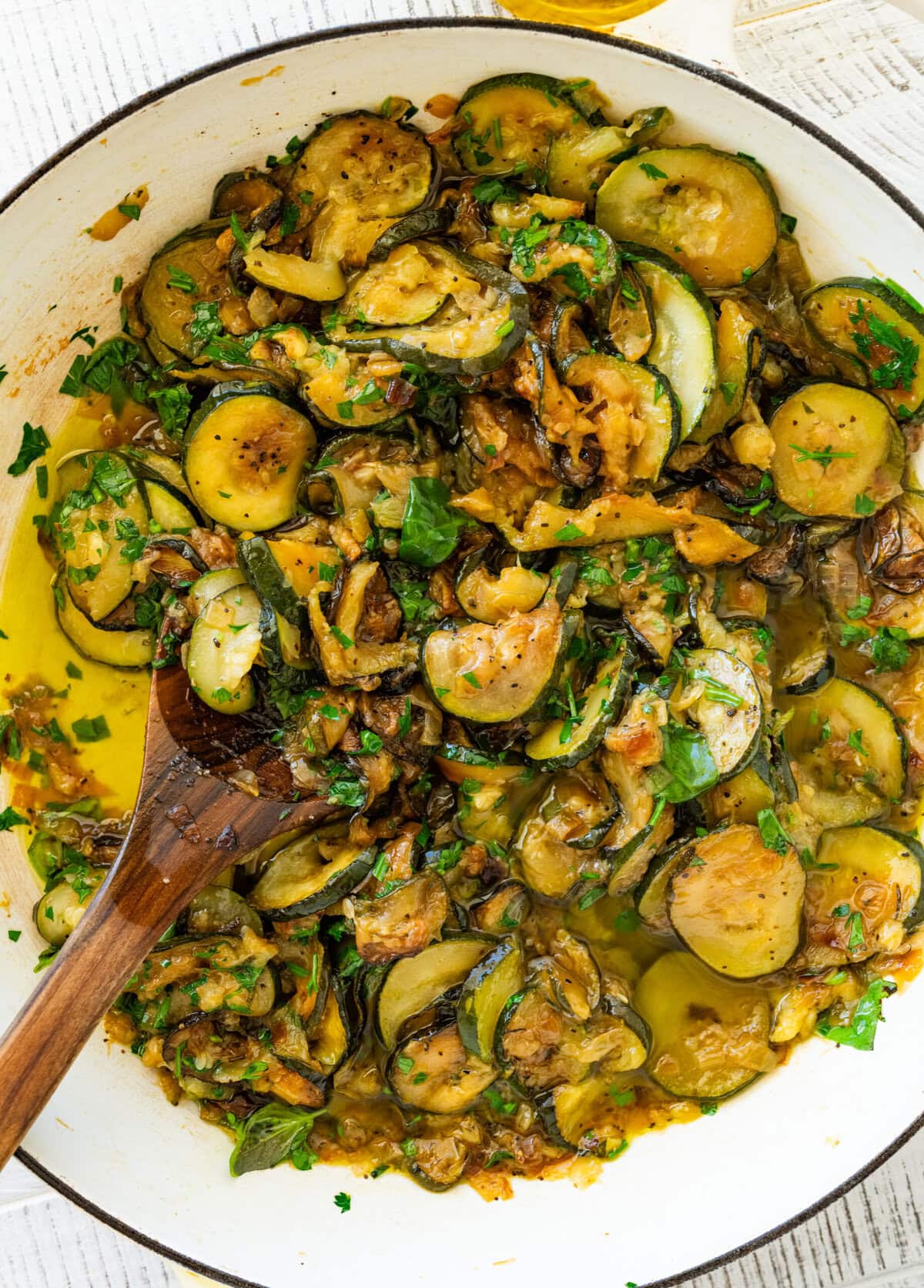 A skillet of fully cooked zucchini and onions with a wooden spoon resting inside.