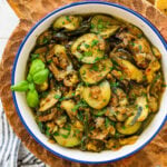 A skillet of sauteed zucchini with onions garnished with basil and parsley.