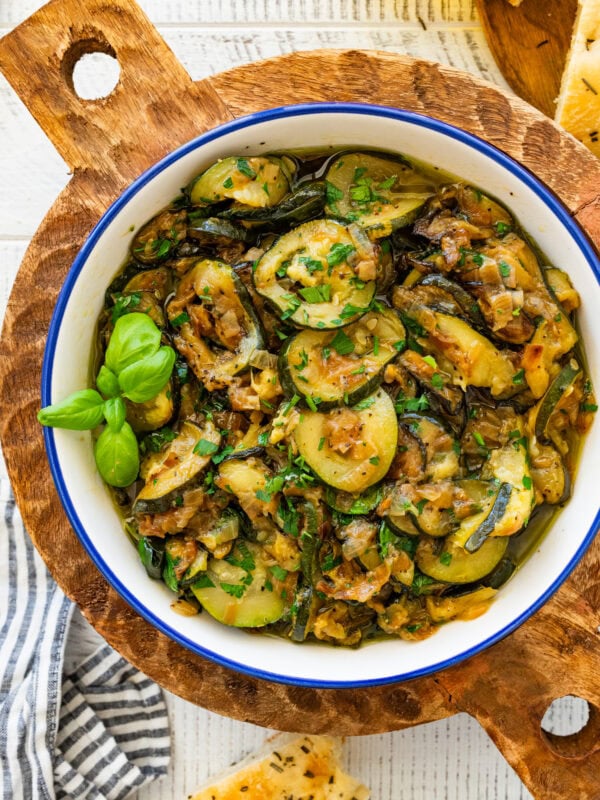 A skillet of sauteed zucchini with onions garnished with basil and parsley.