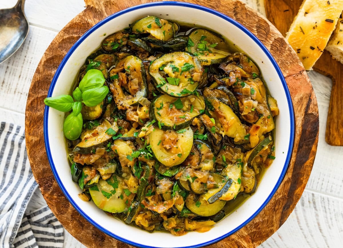 A skillet of sauteed zucchini with onions garnished with basil and parsley.