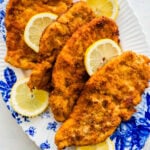 crispy breaded chicken cutlets on a blue and white platter with lemons.